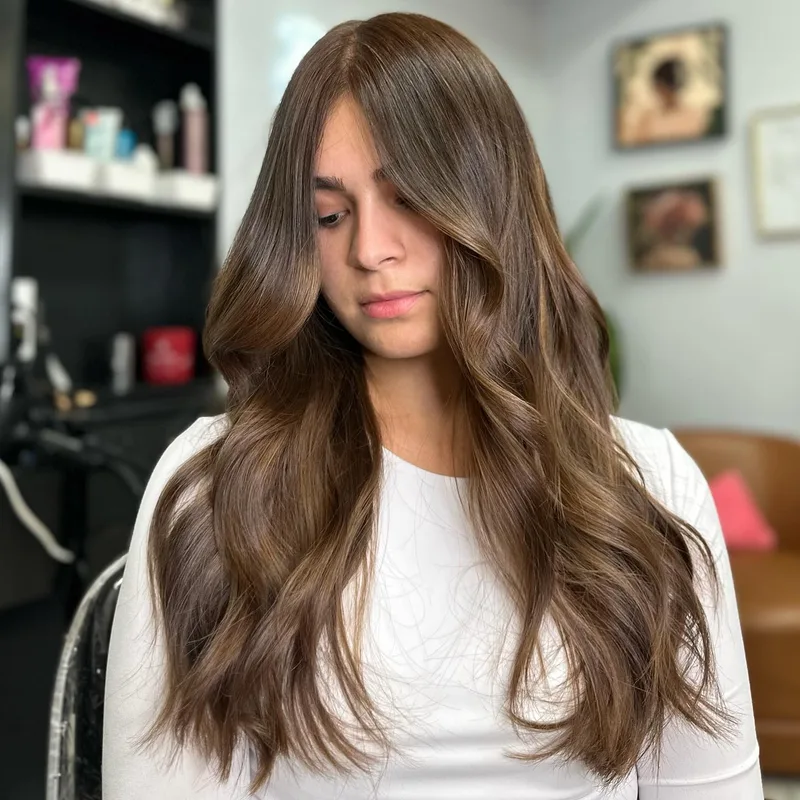 Woman with long brunette waves and lighter face-framing pieces