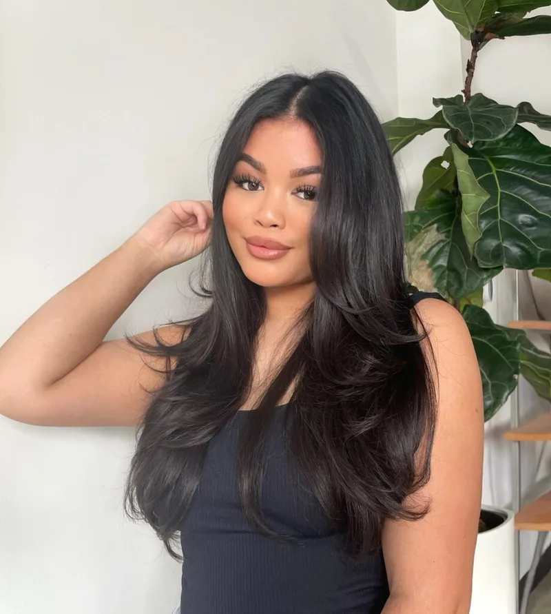 Woman with long dark layered hair curved softly through the ends