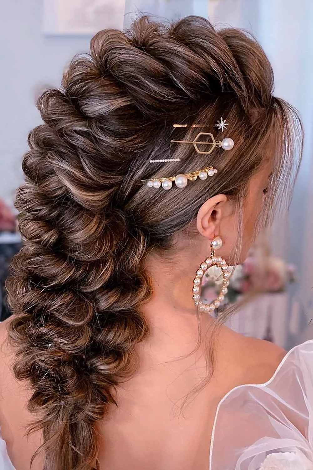 Back-side view of a broad brown braided crest with pearl and geometric pins above the ear