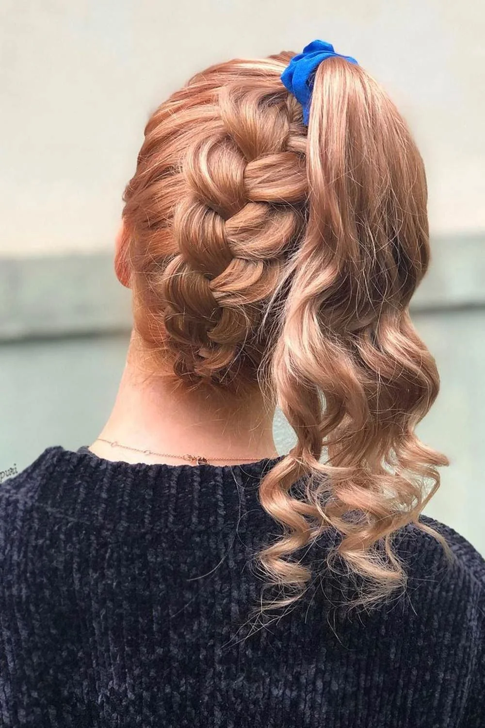Back-side view of a red-haired braid rising toward a curled ponytail with a blue tie