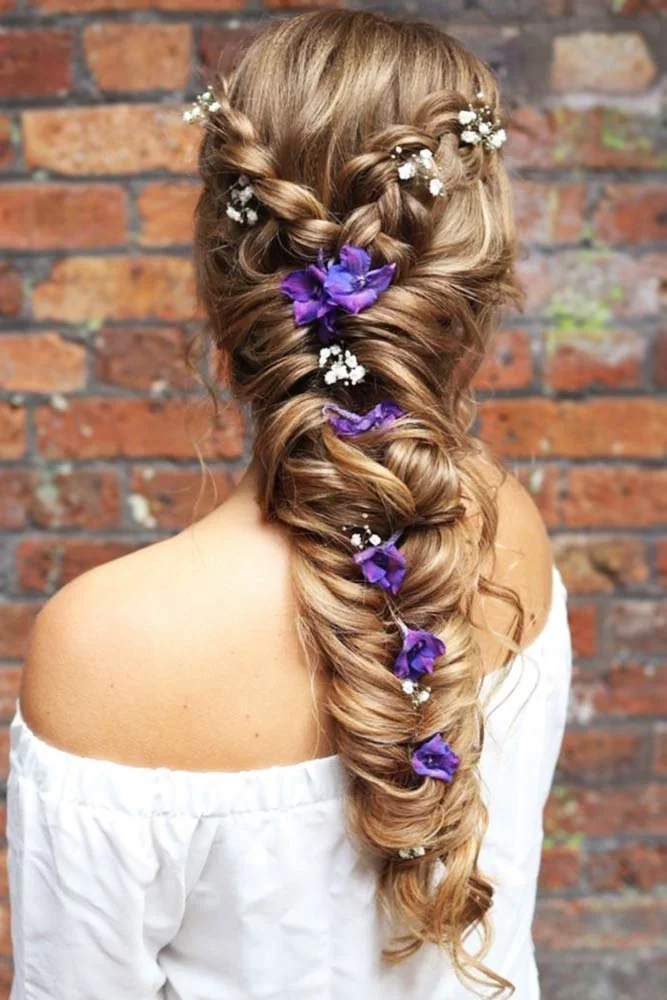 Back view of a broad brown braid with purple flowers and small pale accents