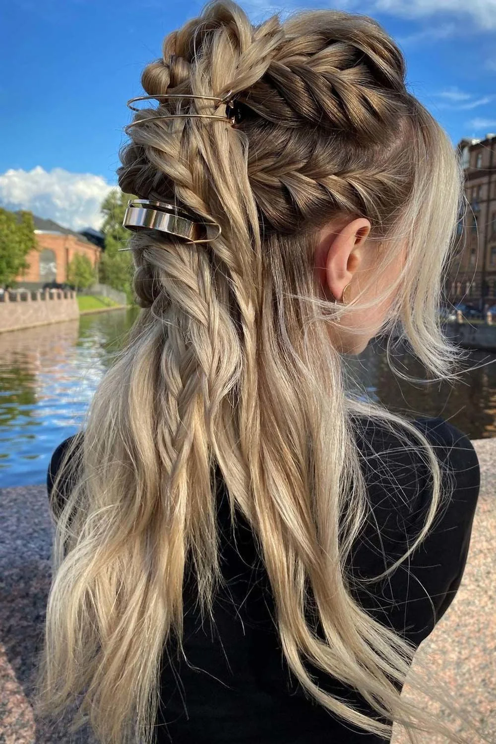 Back-side view of blonde braids meeting over loose waves with visible metal clips