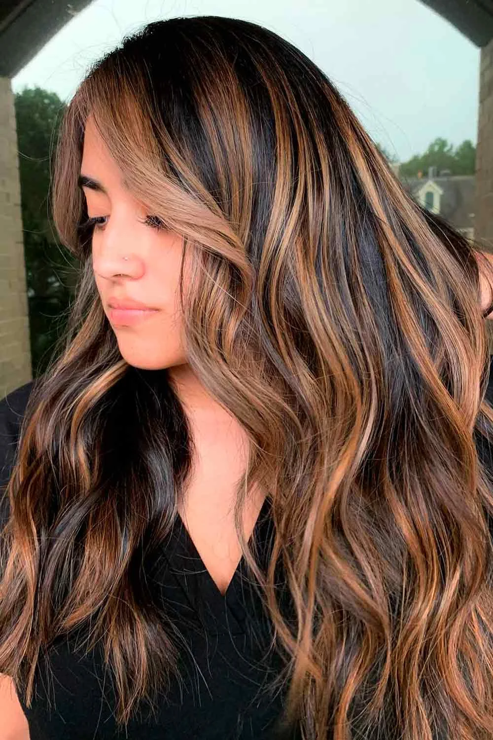 Front-side view of long dark brown waves with broad warm highlights beside the face