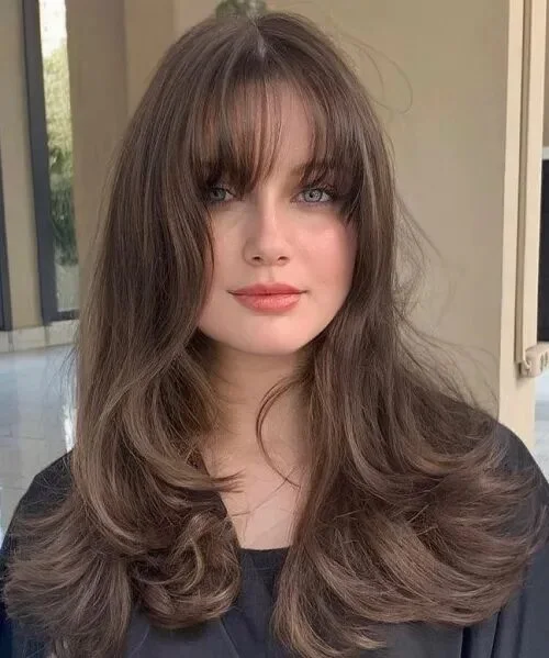 chest wavy brunette layers with wispy fringe shown as a butterfly haircuts with bangs idea