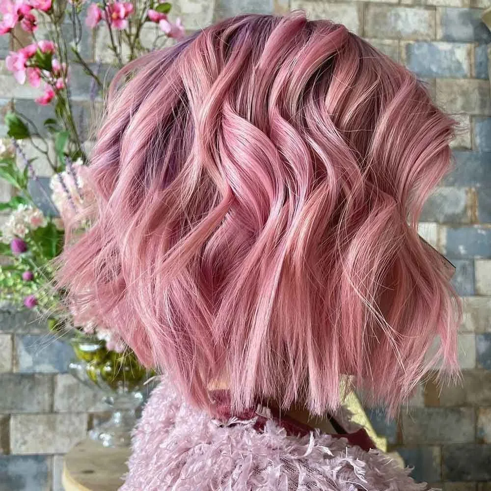 Back-side view of a short wavy bob in muted blush pink with darker shadow at the roots