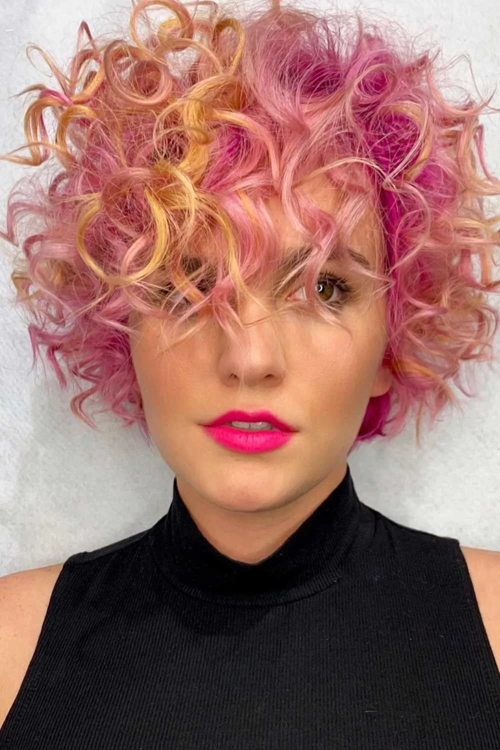 Front portrait of a short curly crop with pink, apricot and golden strands around the face