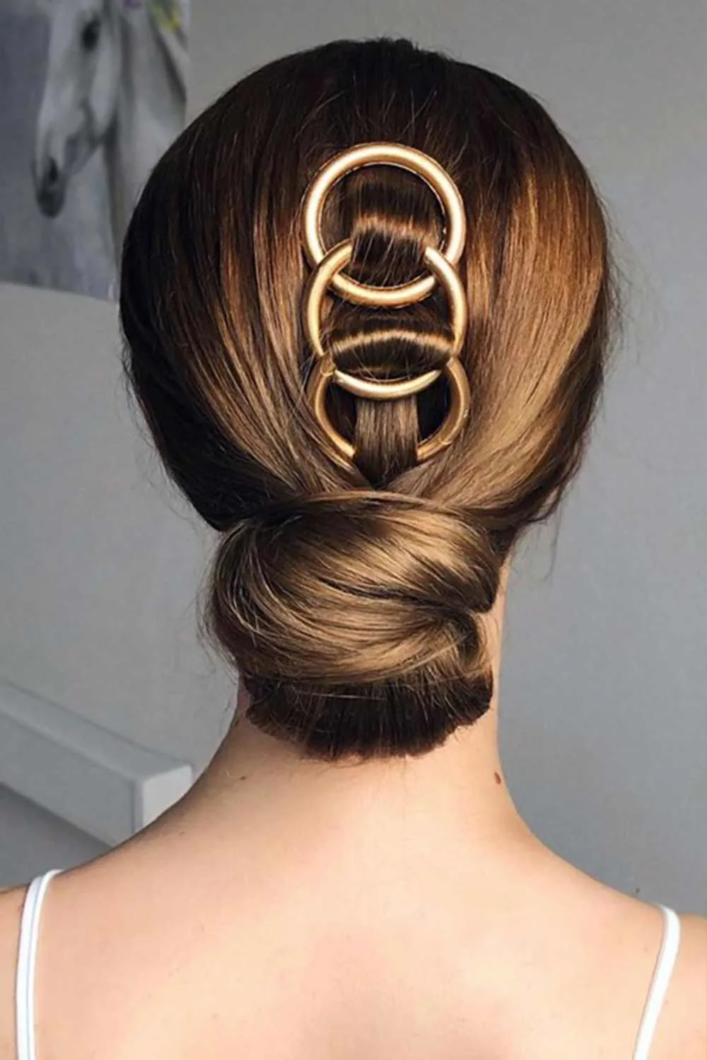 Back view of a smooth brown low bun with three large linked gold hoops down the crown