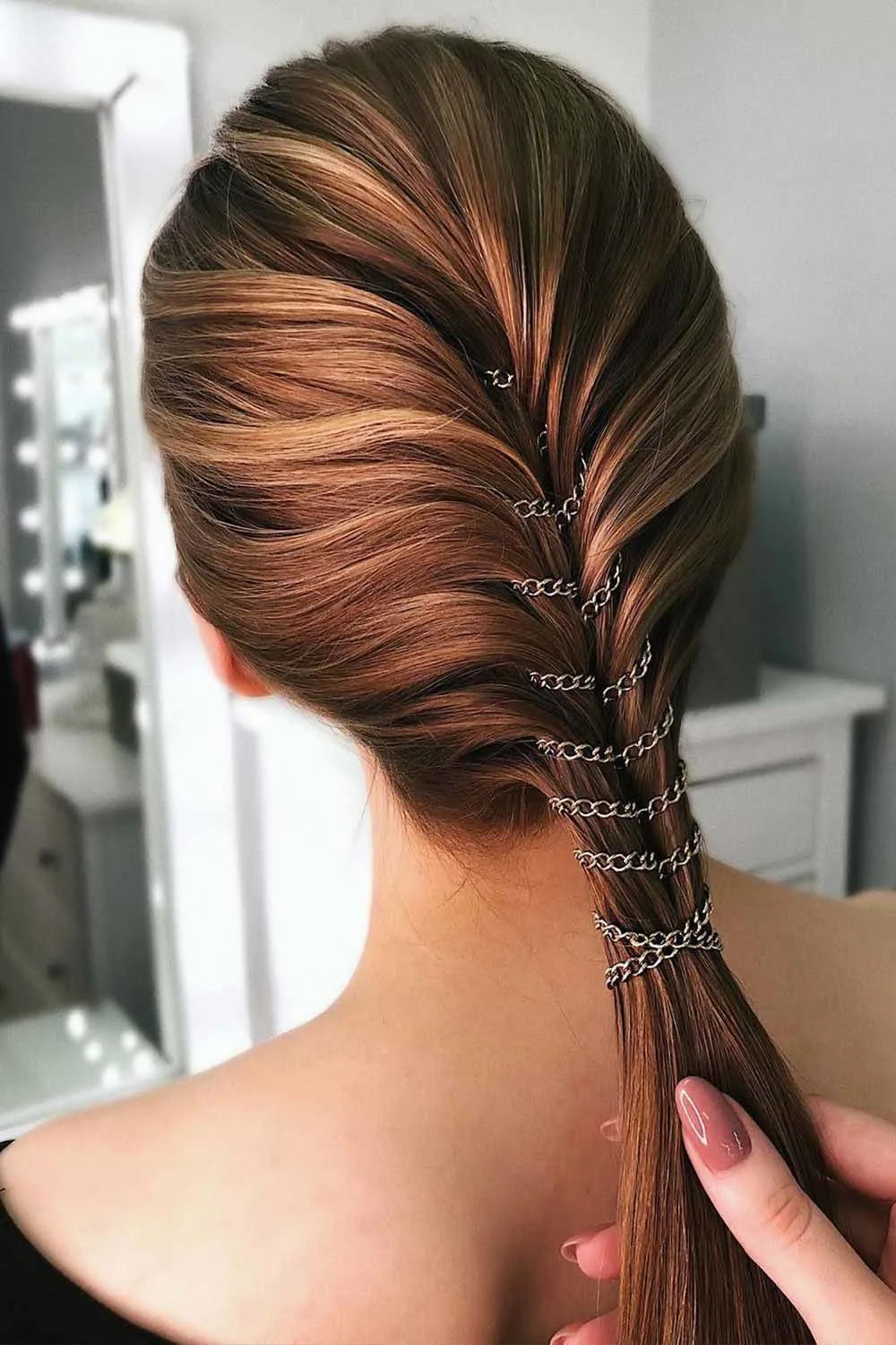 Back-side view of a copper ponytail with a twisted base crossed by fine dark metal chains