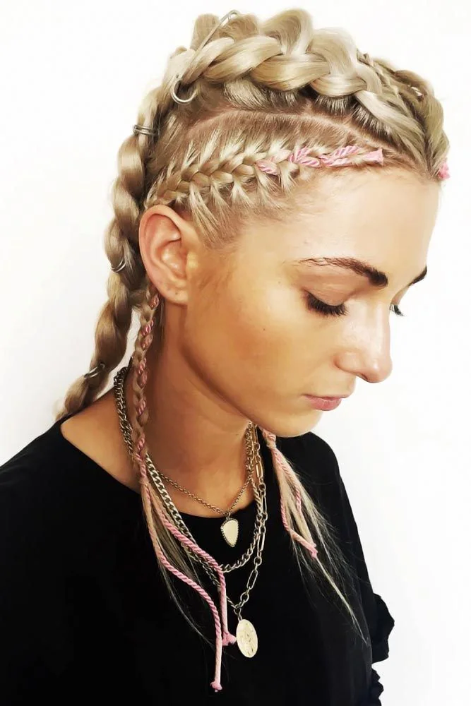 Side portrait of blonde hair with raised crown braids, pink accent strands and gold rings