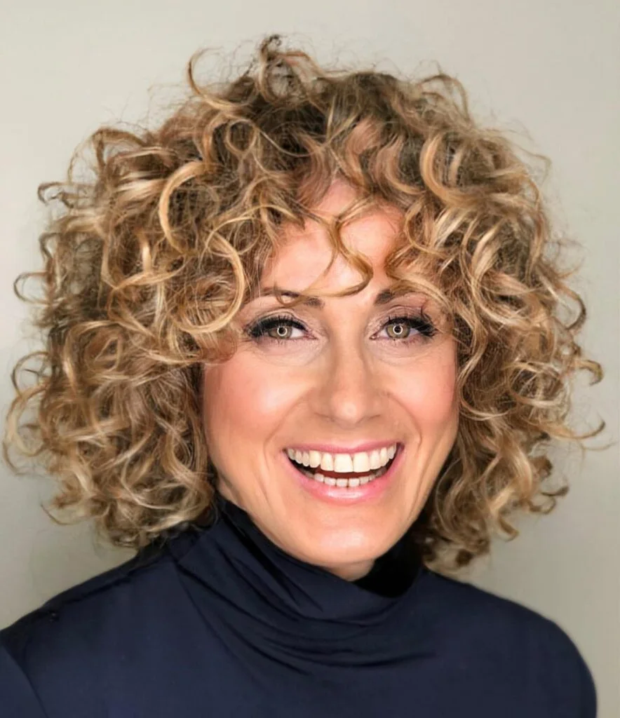 Defined silver curls with short rounded volume and a soft face-opening shape. This hairstyle is shown as inspiration for women over 60 with thin hair.
