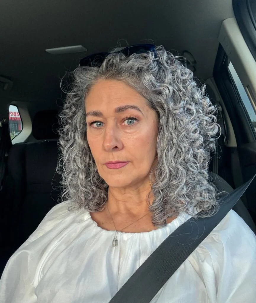 A soft gray curly bob with natural volume, rounded sides, and a neck-length shape. This hairstyle is shown as inspiration for women over 60 with thin hair.