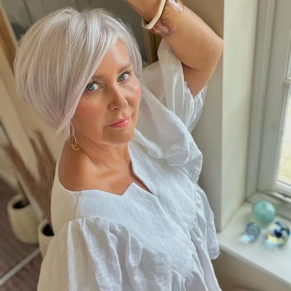 A side-part silver bob with a compact neck-length line and smooth movement near the cheek. This hairstyle is shown as inspiration for women over 60 with thin hair.