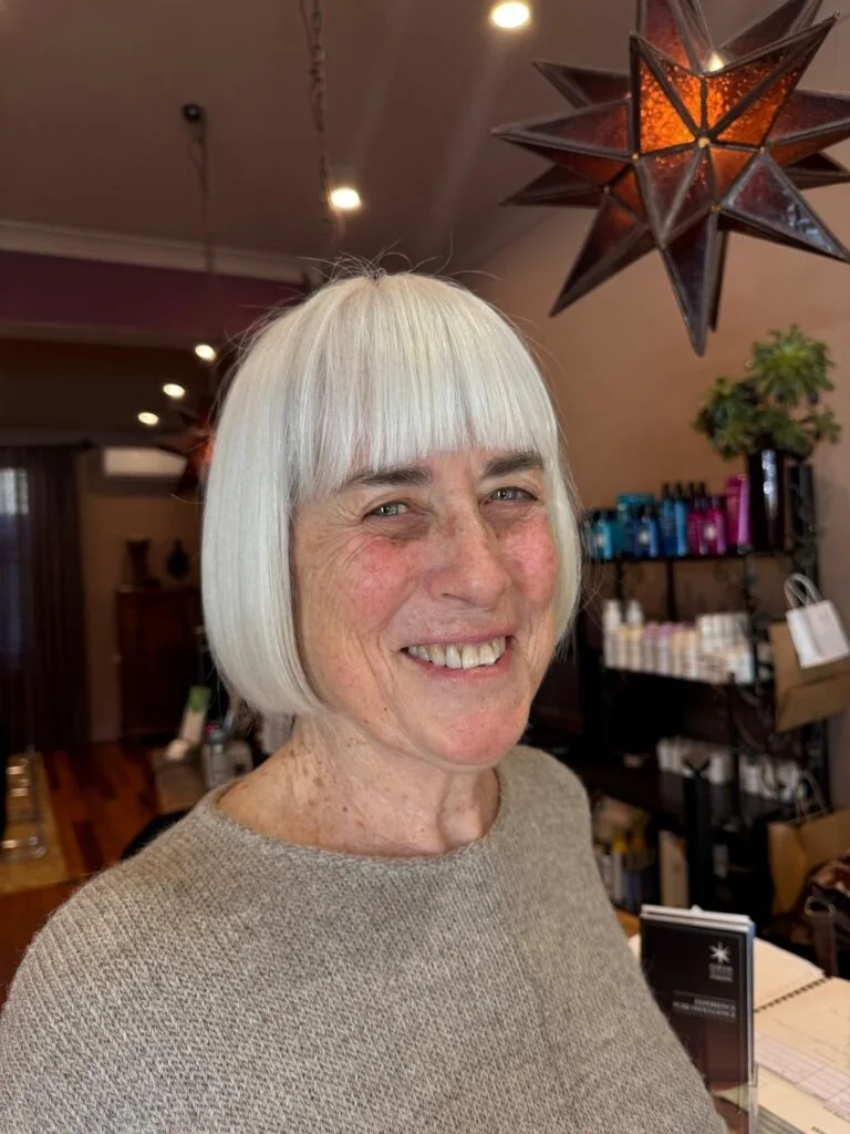 A blunt white bob with full bangs, a smooth chin-length edge, and a bright finish. This hairstyle is shown as inspiration for women over 60 with thin hair.