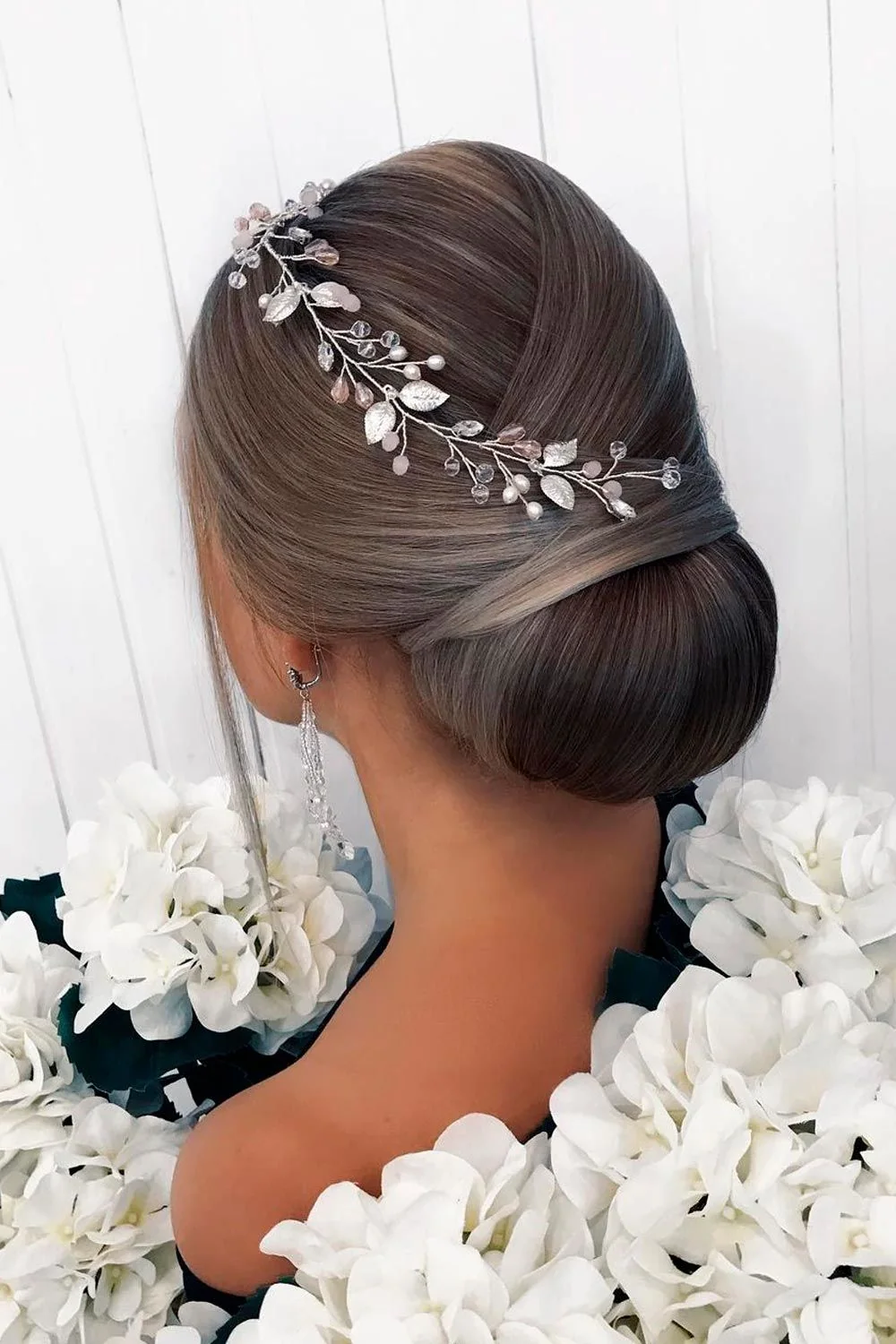 Back-side view of a smooth brunette low bun with a silver pearl vine sweeping across the crown