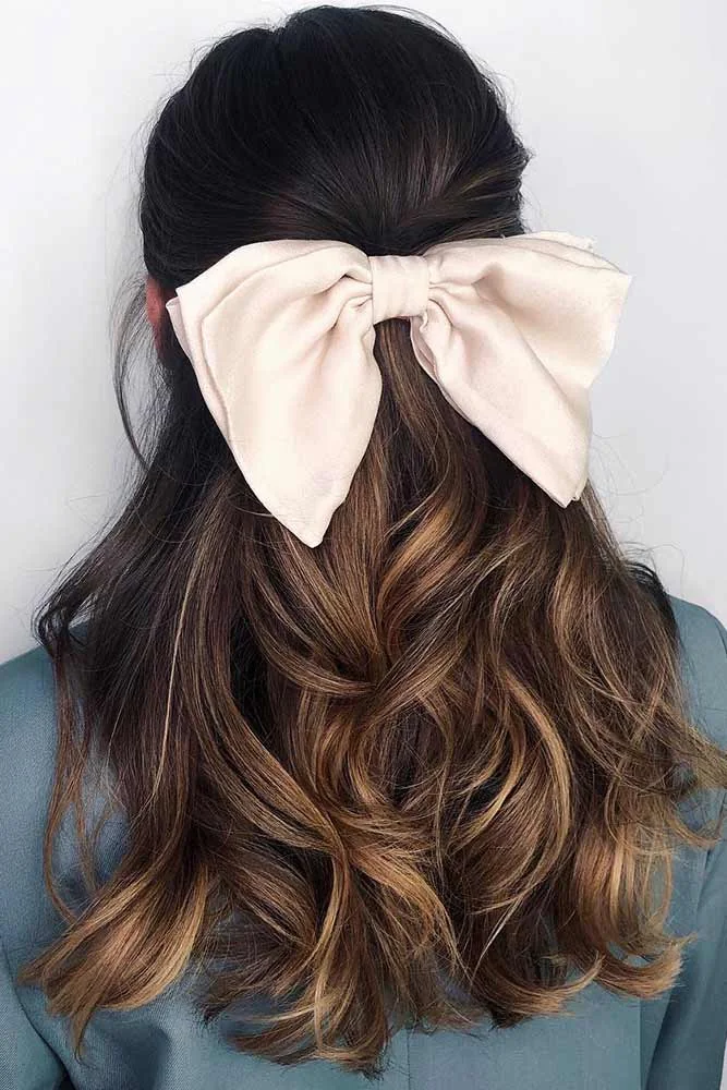 Back view of dark long waves gathered half up beneath an oversized cream fabric bow