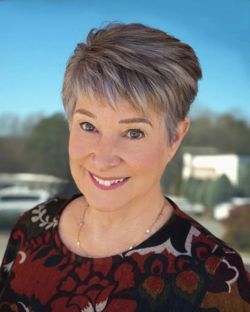 Older woman with a short golden pixie, textured top, and layered side fringe