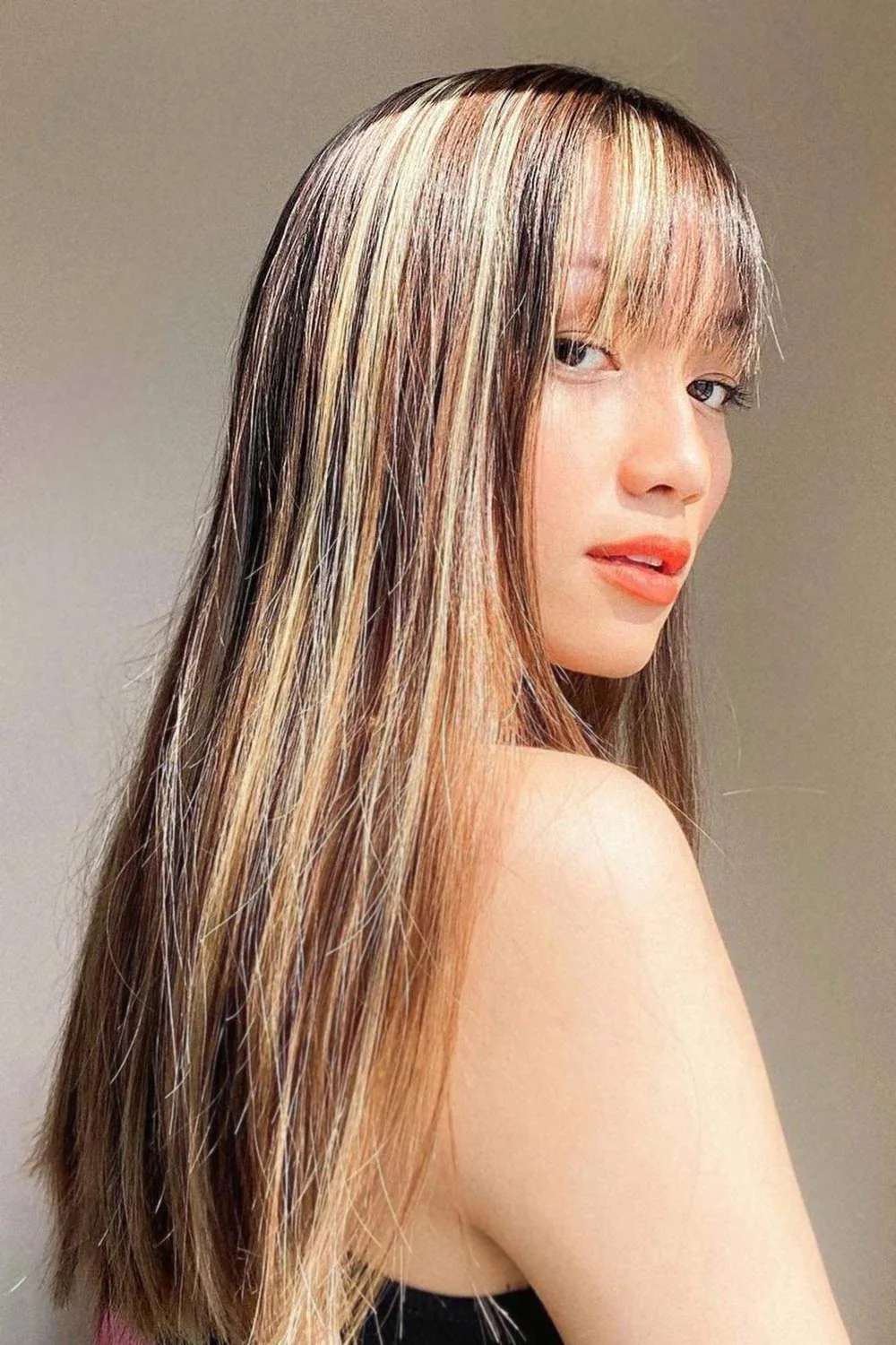 Side-front view of long straight highlighted brown hair with fine bangs