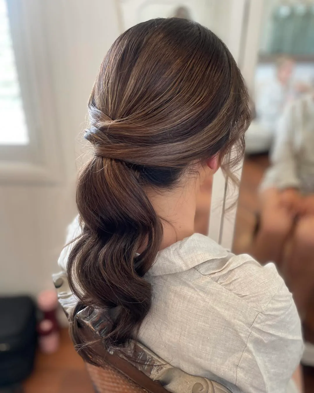 chest wavy brunette ponytail shown as a low ponytail hairstyles idea, featuring glossy finish, shown in soft brunette twisted low ponytail
