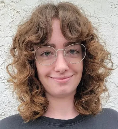 Glasses-friendly medium curly shag haircut with bangs and rounded texture for thin fine hair