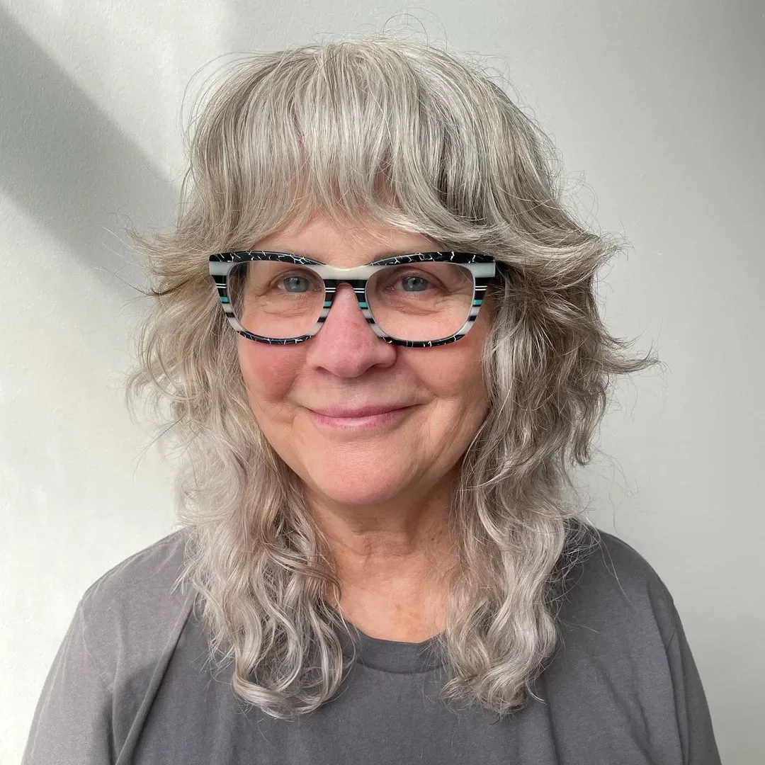 Silver wavy medium shag haircut with glasses and soft curtain bangs for thin fine hair