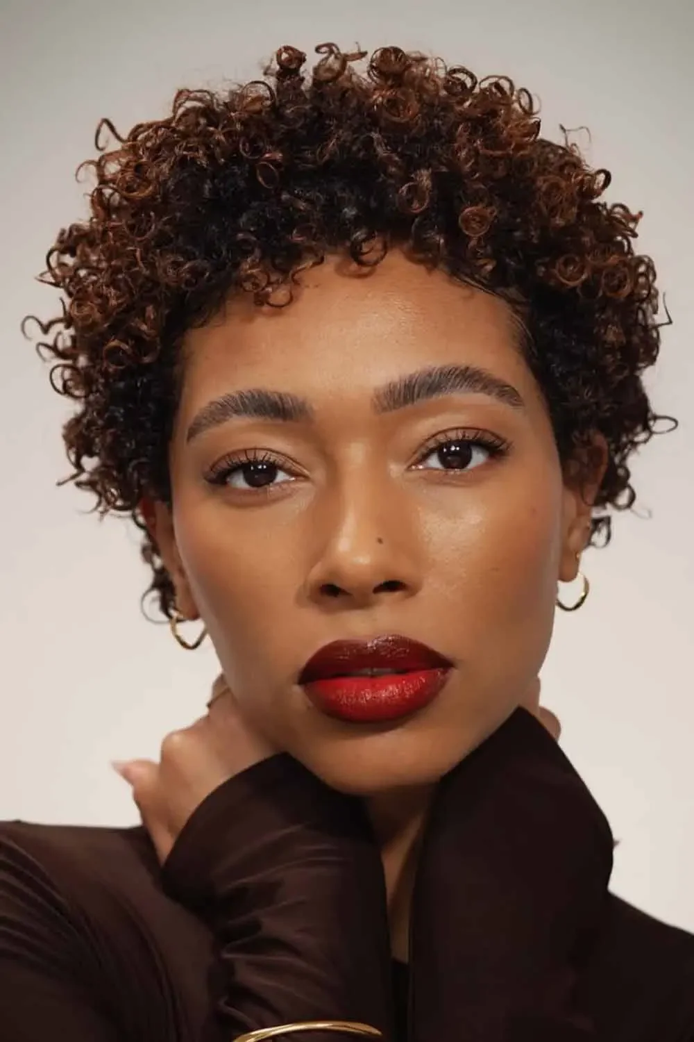 Deep brunette curly pixie cut with short bangs and rounded texture