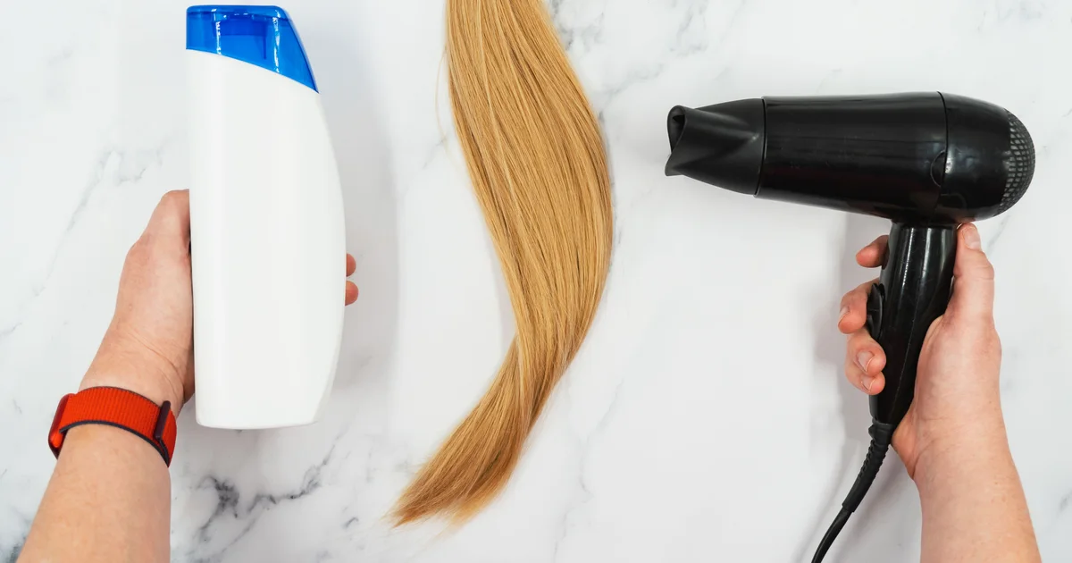 Flat lay of a hair-care bottle, blonde hair section, and handheld hair dryer