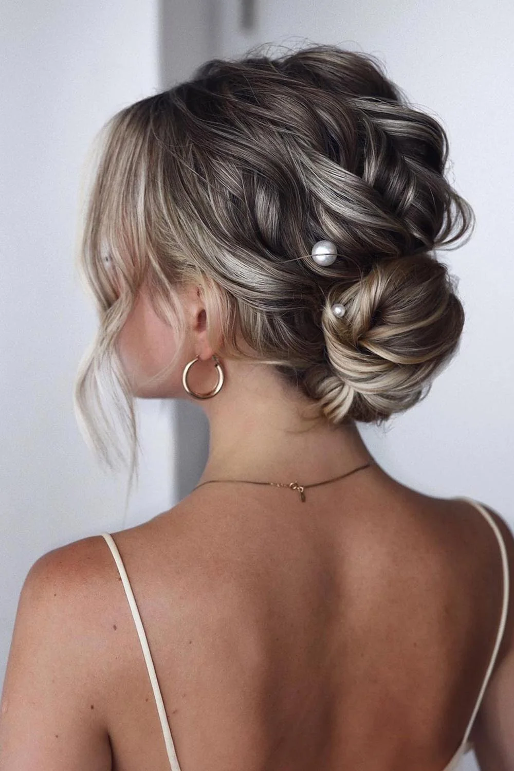 Ashy brown-blonde hair gathered into a low rounded bun with loose front pieces