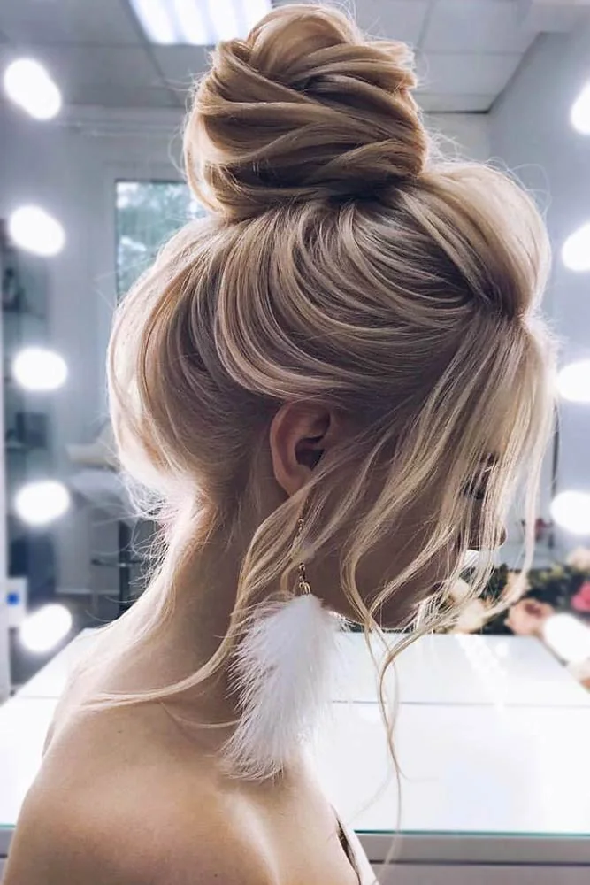 Blonde hair swept into a high wrapped knot with a loose front section