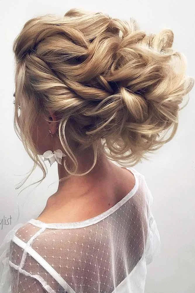 Blonde hair swept into a broad interlaced updo with curled front strands