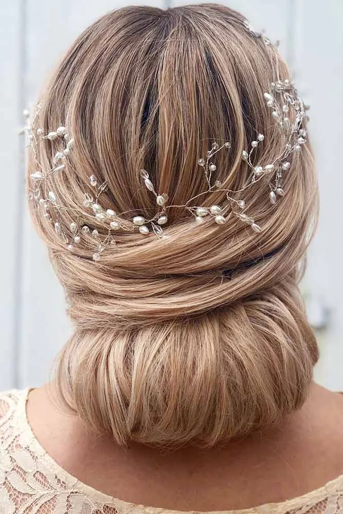 Blonde hair gathered into a smooth low rounded roll beneath a pearl-like hair vine