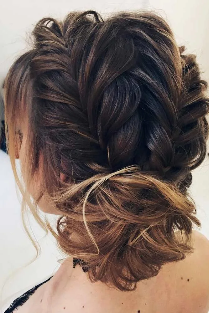 Dark hair with a raised back braid leading into a low tousled bun