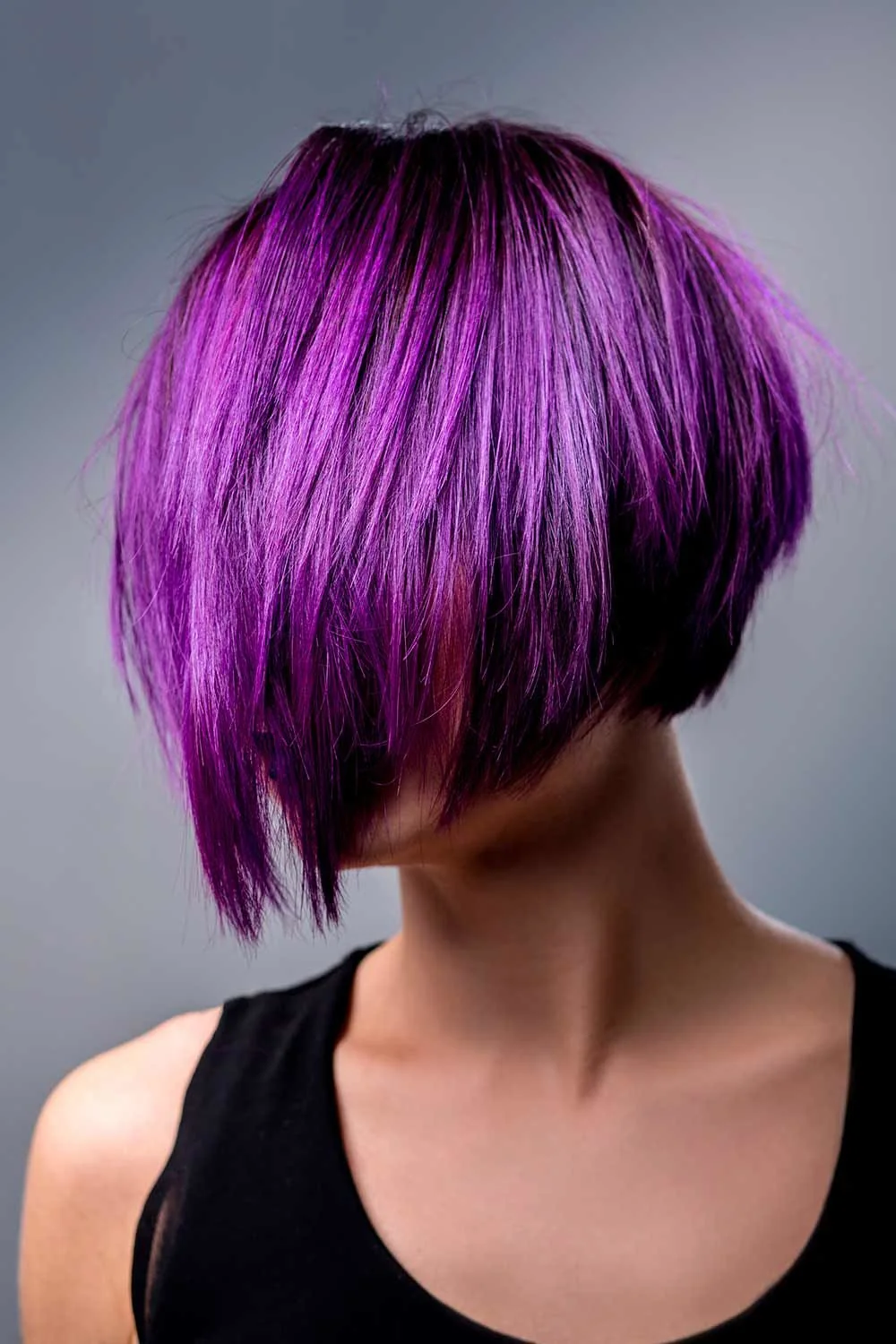 Angled violet bob with dark roots and long front sections swept across the face