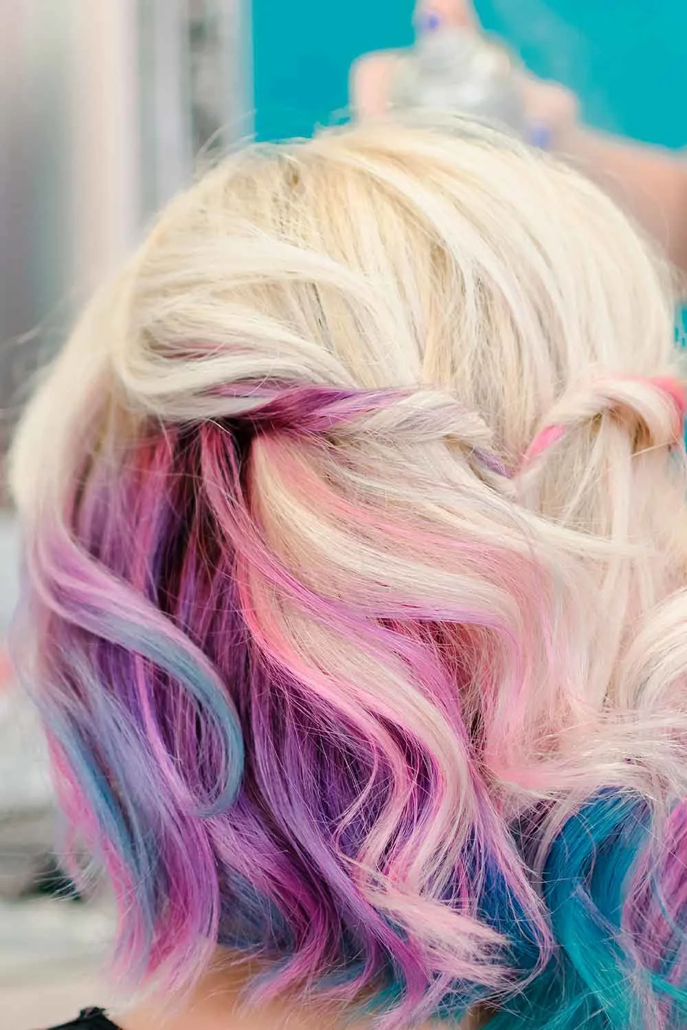 Back view of a short blonde wavy bob with pink and lilac color visible underneath the top layer
