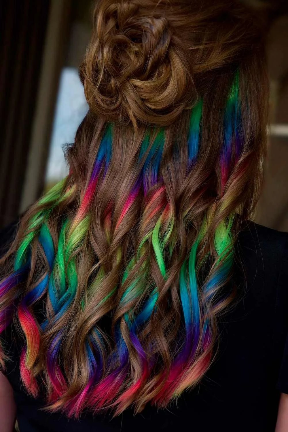 Back view of long brown curls with multicolor sections exposed beneath a small gathered top
