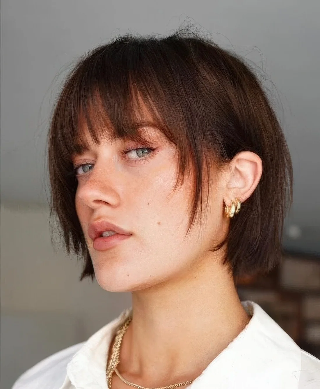 Blunt dark brunette bob with wispy bangs and face-framing layers.