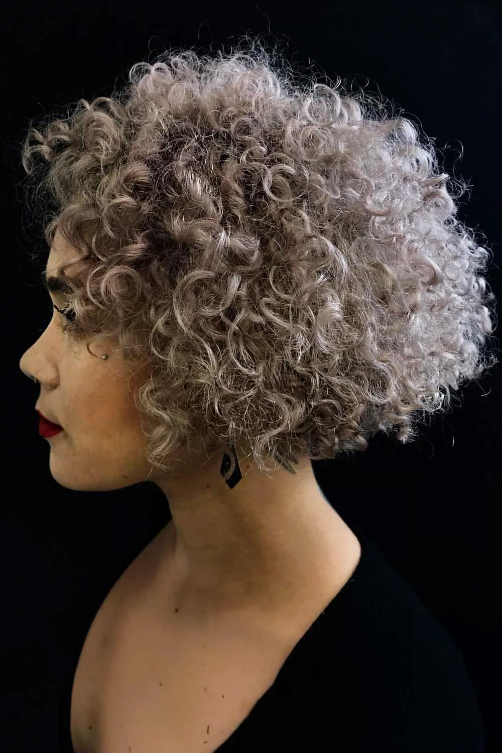 Side view of a rounded short haircut with brown-gray ringlets