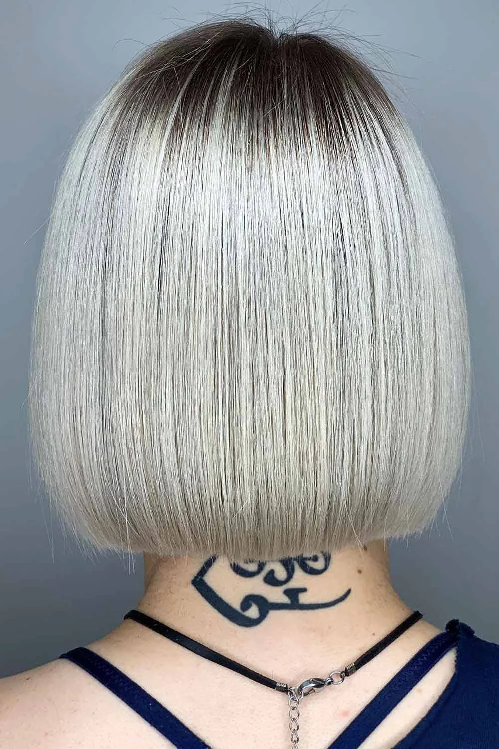Back view of a smooth silver bob with dark roots and a blunt nape-length edge