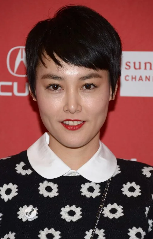 black micro pixie with a short uneven fringe and close sides around the ears on a round face with thin hair