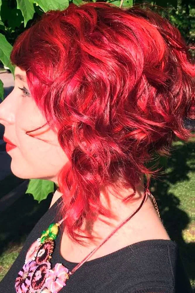 Side view of a short curly haircut in vivid scarlet red with a soft rounded outline