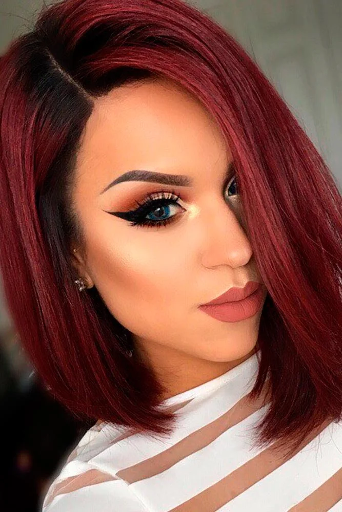 Side portrait of a sleek chin-length wine-red bob with a longer front point and dark roots