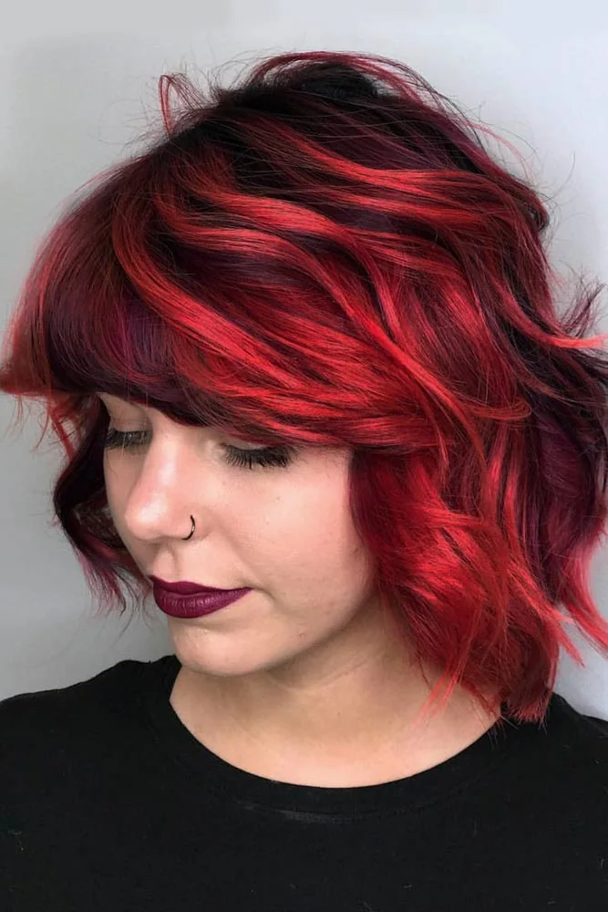 Front-side portrait of a short wavy bob with ruby-red side fringe and deeper burgundy layers