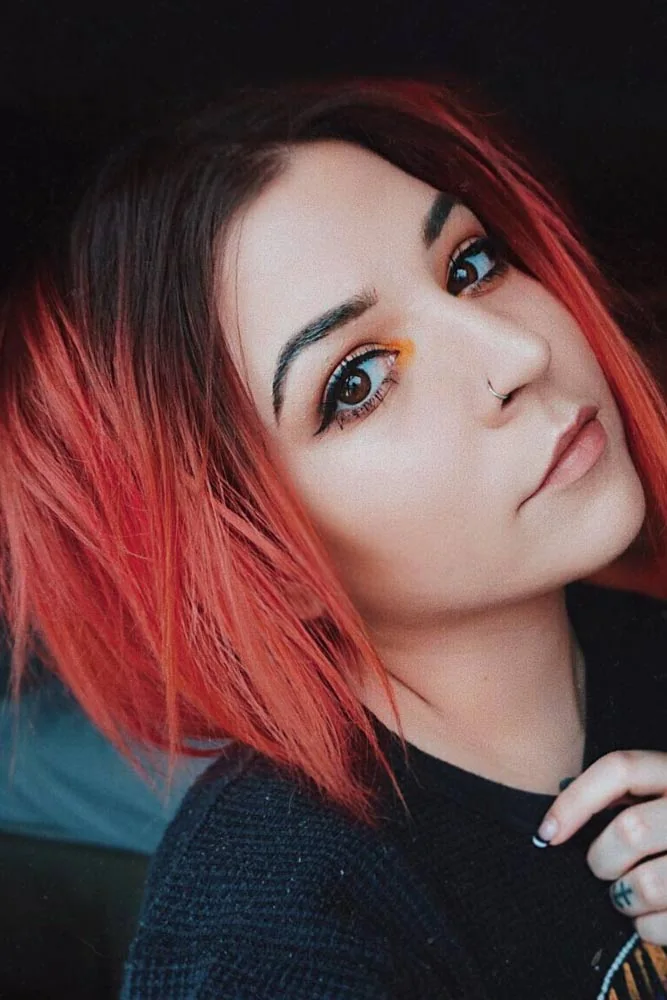 Portrait of a short bob with black roots fading through dark red into coral-pink ends
