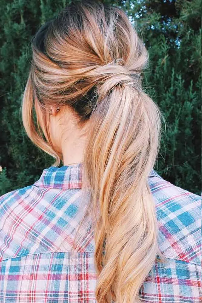 Back view of a loose blonde low ponytail with darker roots and a softly swept crown