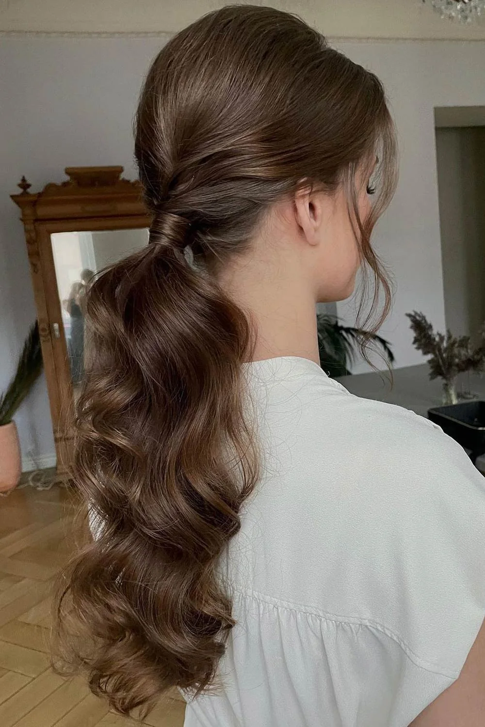 Back-side view of brown hair with side twists joining a low wavy ponytail
