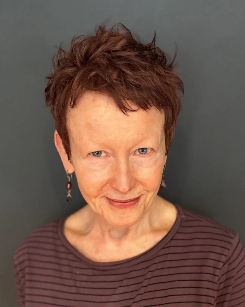 tiny auburn pixie on a woman over 60 with an easy wash-and-wear haircut shape