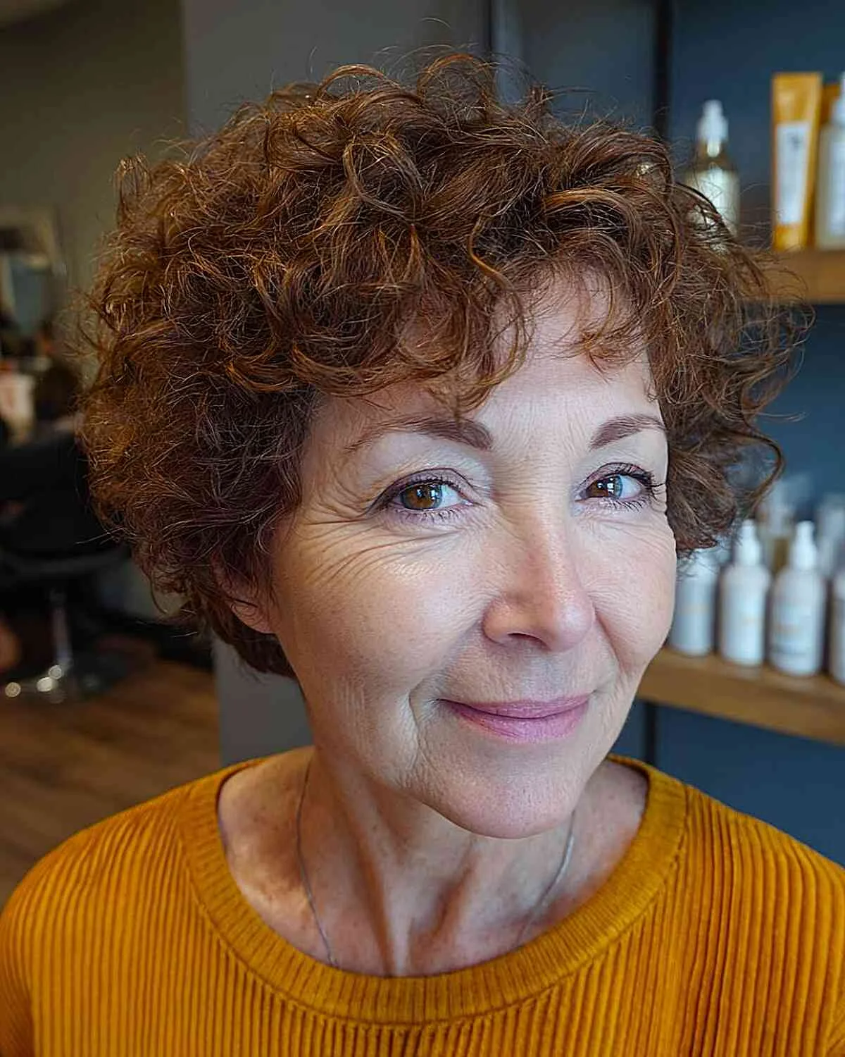 auburn curly crop with bangs on a woman over 60 with an easy wash-and-wear haircut shape