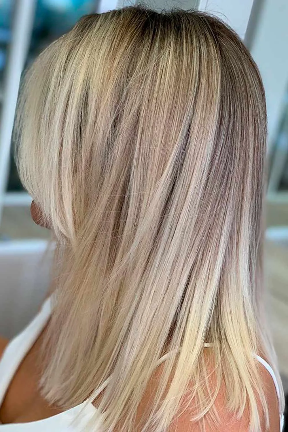 Back-side view of a straight shoulder-length lob with cool ash-blonde lengths and a darker root area