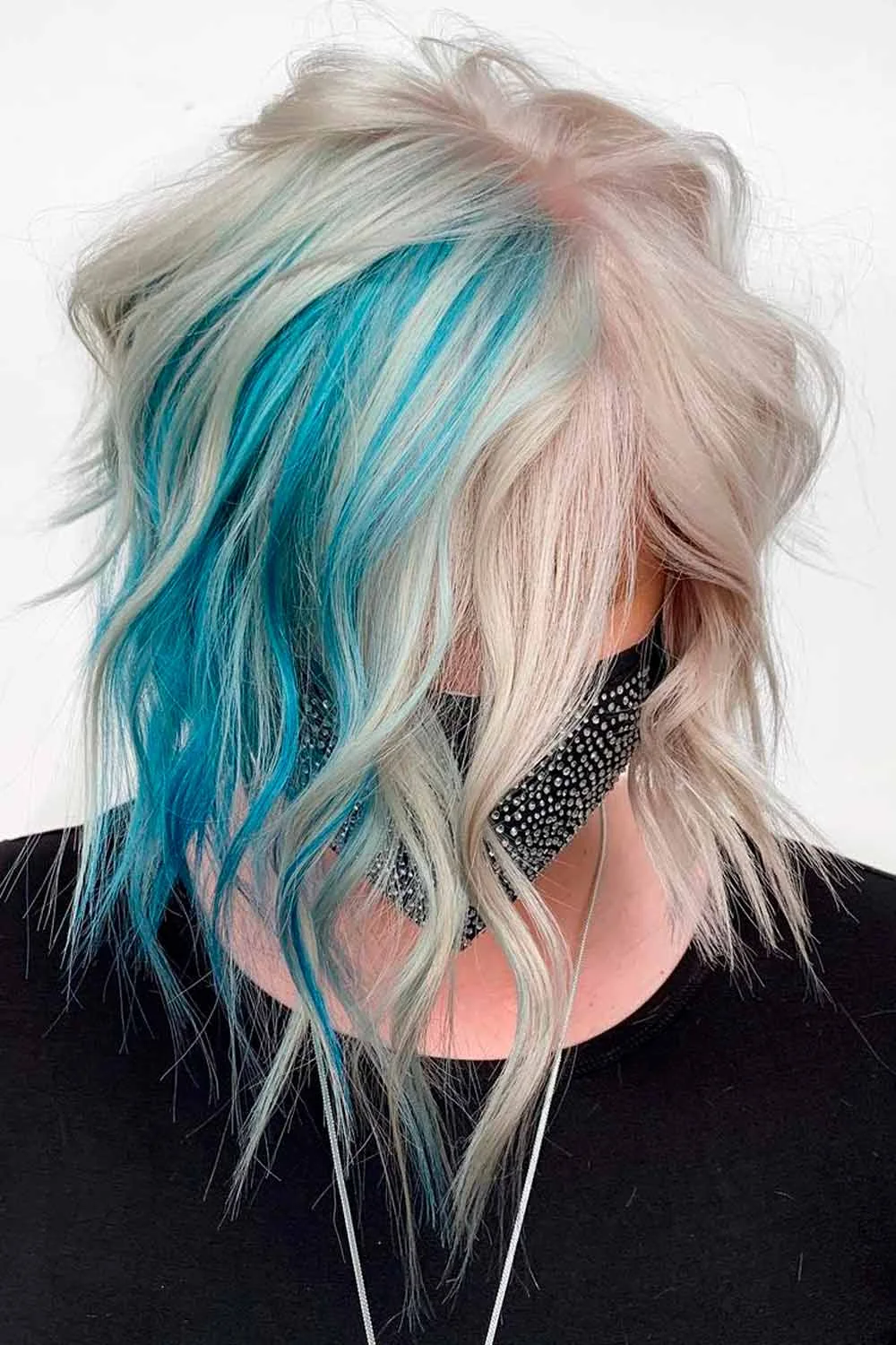 Side view of a pale blonde layered cut with a vivid teal panel beneath the front layers