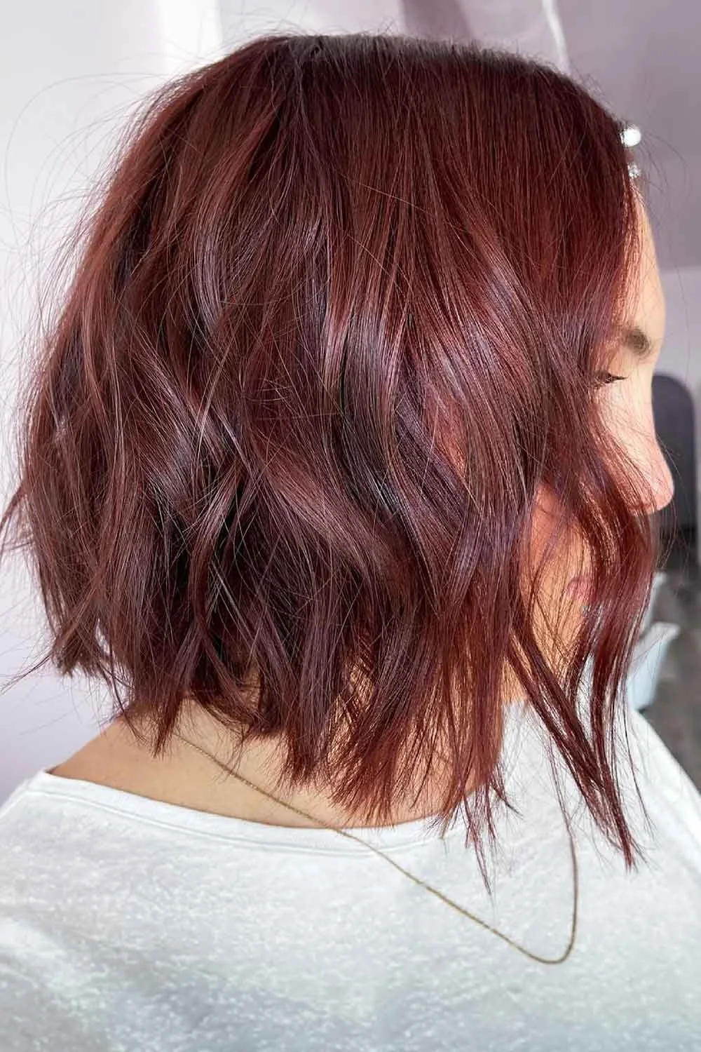 Side-back view of a short textured bob with wine-red color and deeper dark roots
