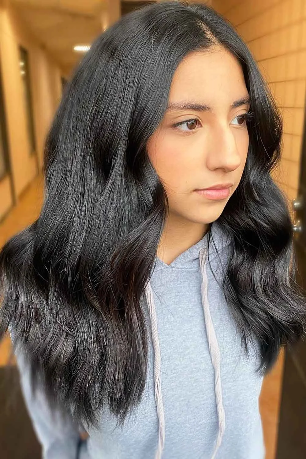 Woman with long soft-black waves and a smooth center-parted crown